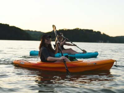 woman in blue shirt and blue denim jeans riding orange kayak on water during daytime